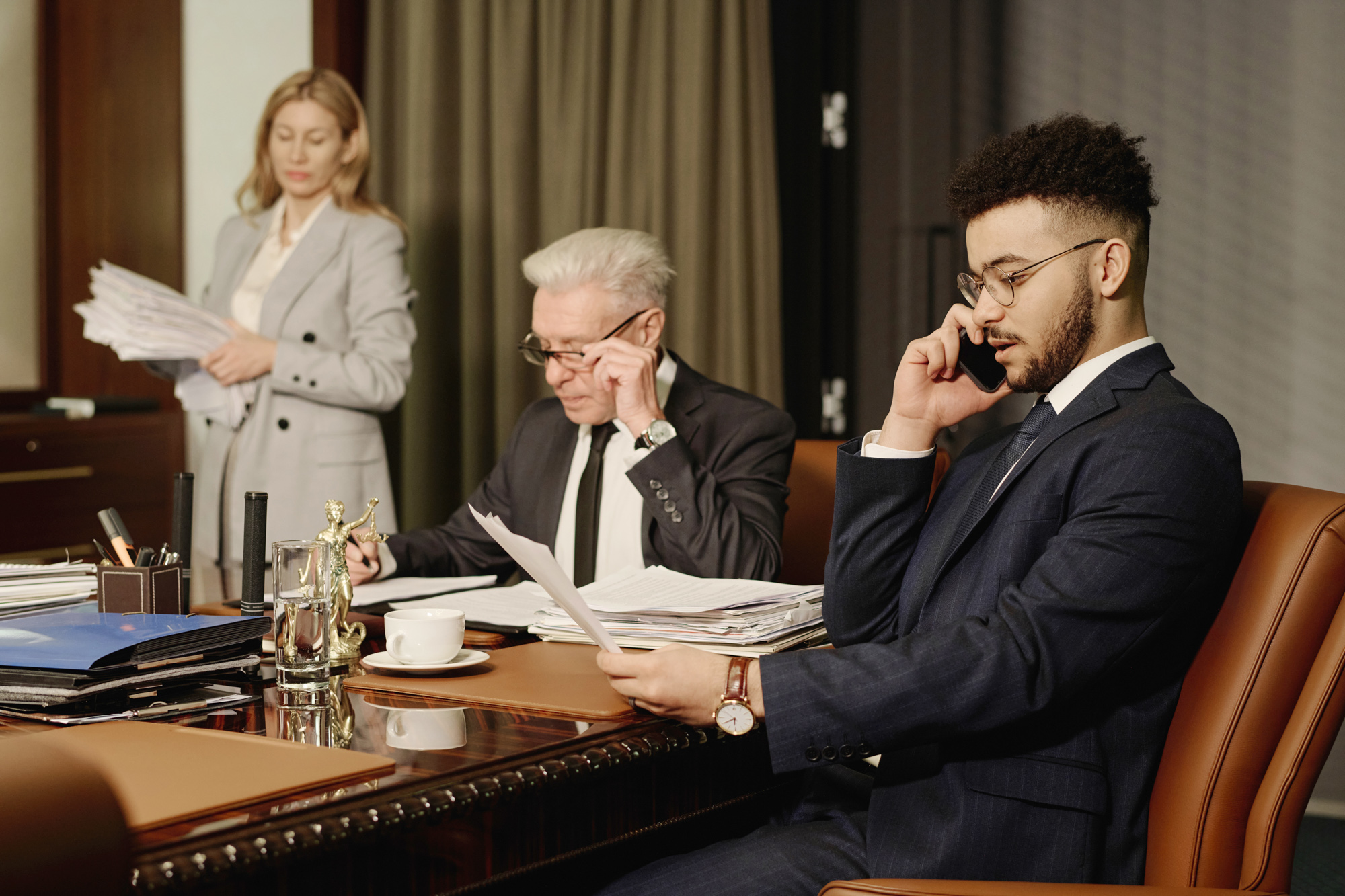 Three people going over paperwork while one nearest camera is on the phone.